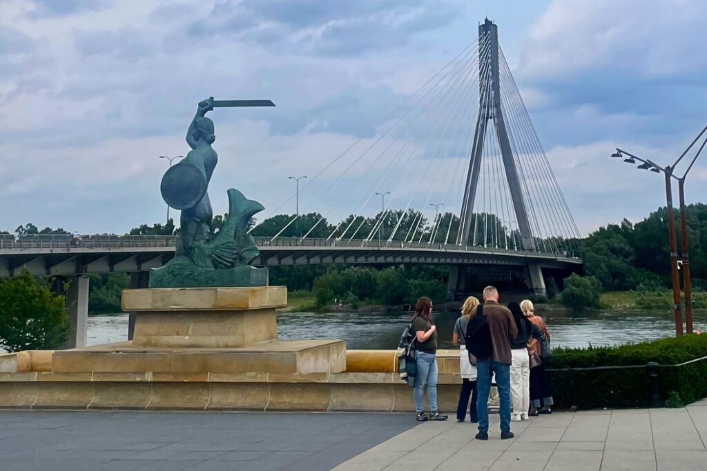 Grupa uczestników gry miejskiej nad Wisłą przy Syrence Warszawskiej podczas wydarzenia firmowego